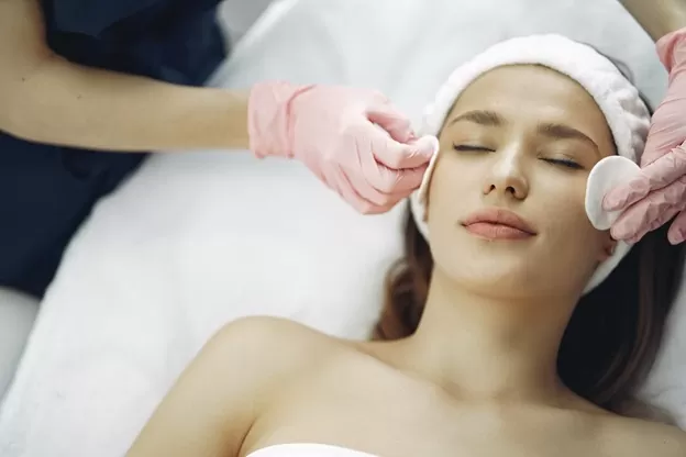 A professional prepping a woman’s skin for dermablading procedure